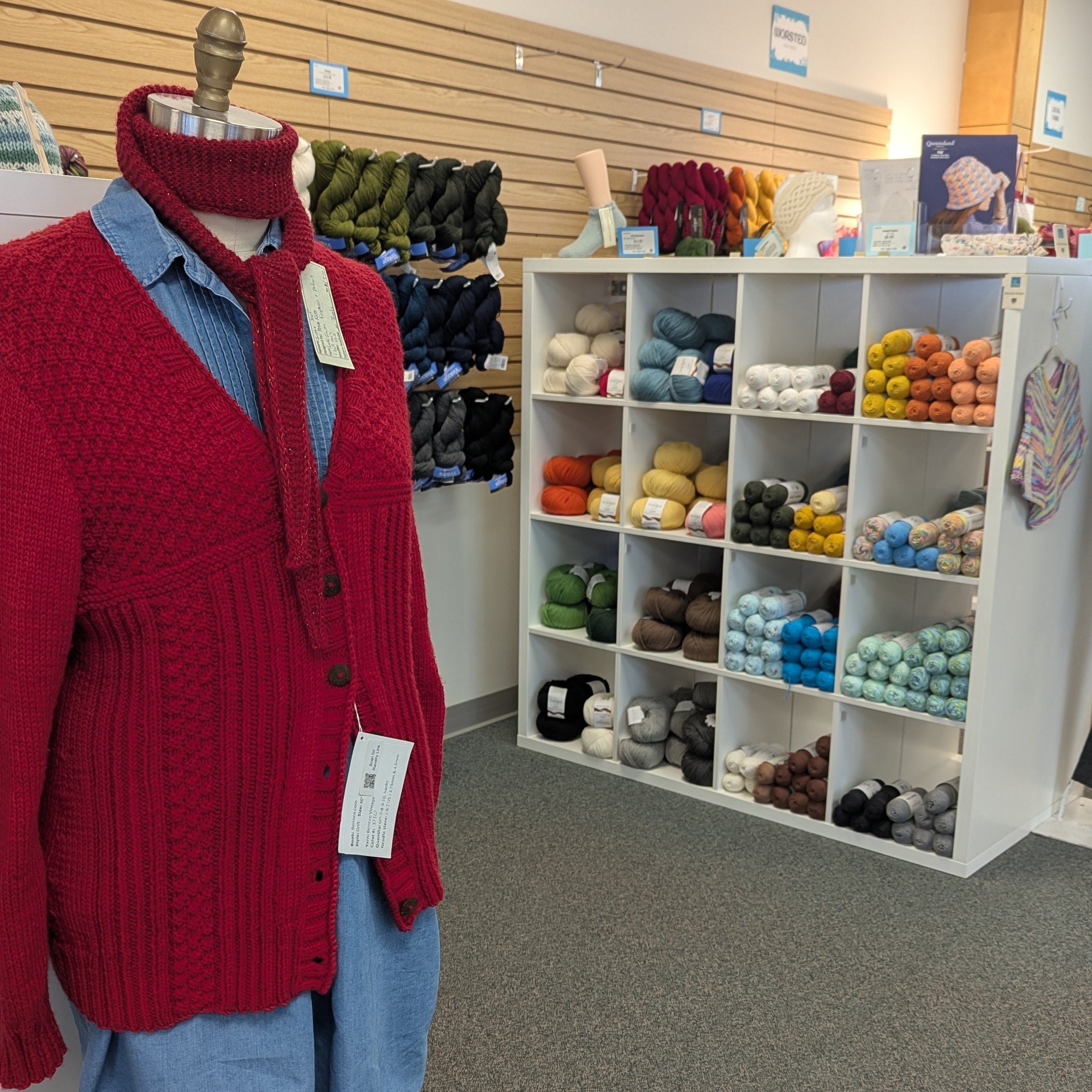 Red sweater and blue skirt on a mannequin in a store with shelves of products in the background.